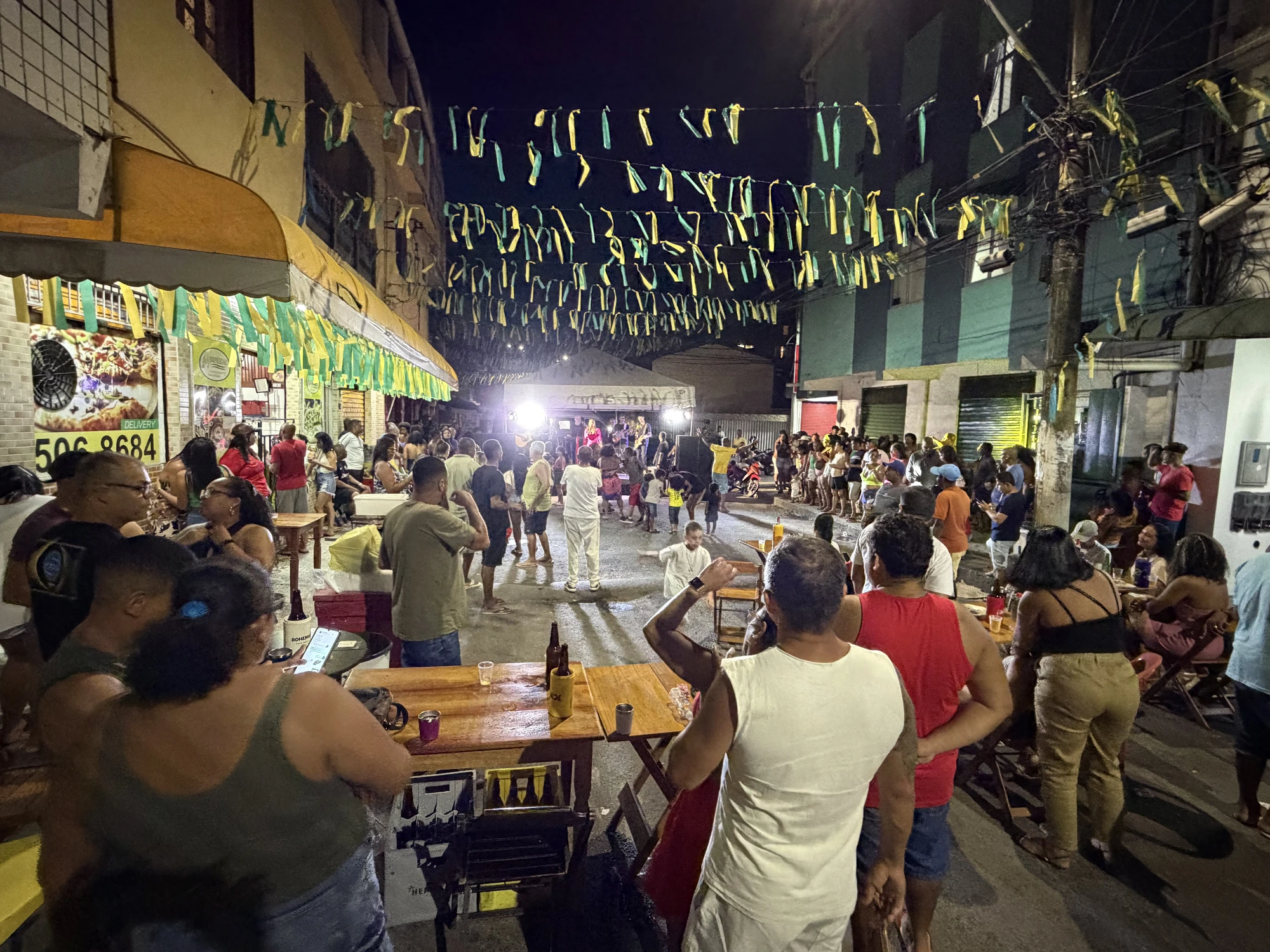 Banda tocando ao vivo em Pituaçu — Salvador, decoração verde e amarela, público lotando os bares da rua